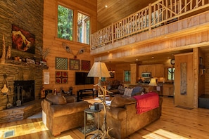 A spacious log cabin interior with a fireplace, a cozy seating area, a dining table, and a kitchen.