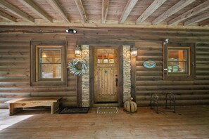 A log cabin with a wooden door, stone accents, a wreath, and a welcome mat.