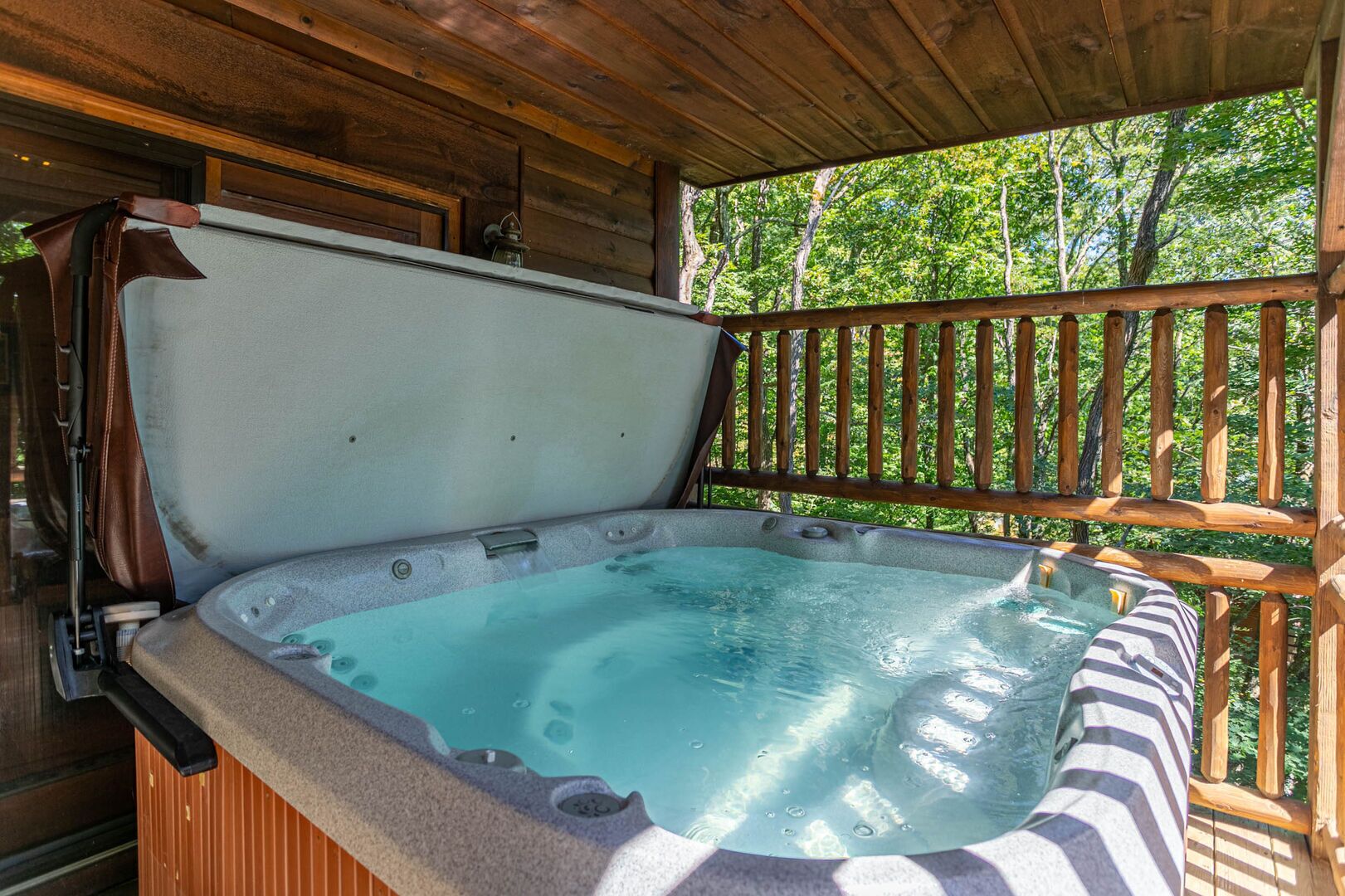 Un bain à remous doté d’une terrasse et d’une rambarde en bois, entouré d’arbres.