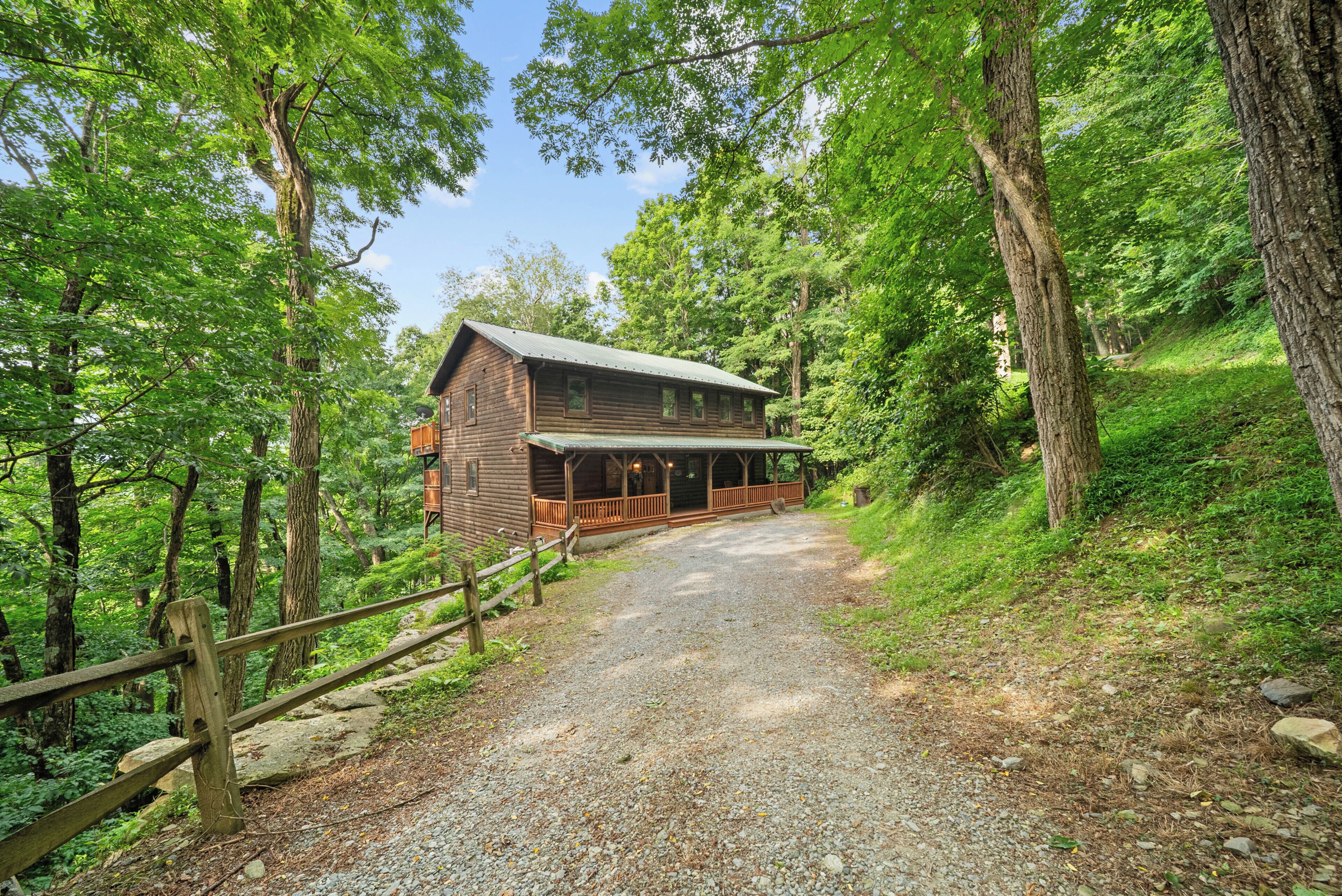 A wooden cabin with a porch, surrounded by trees and a gravel path.