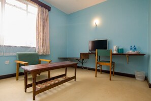 Quarto com uma mesa de madeira, duas cadeiras, uma televisão e uma estante com garrafas de água.