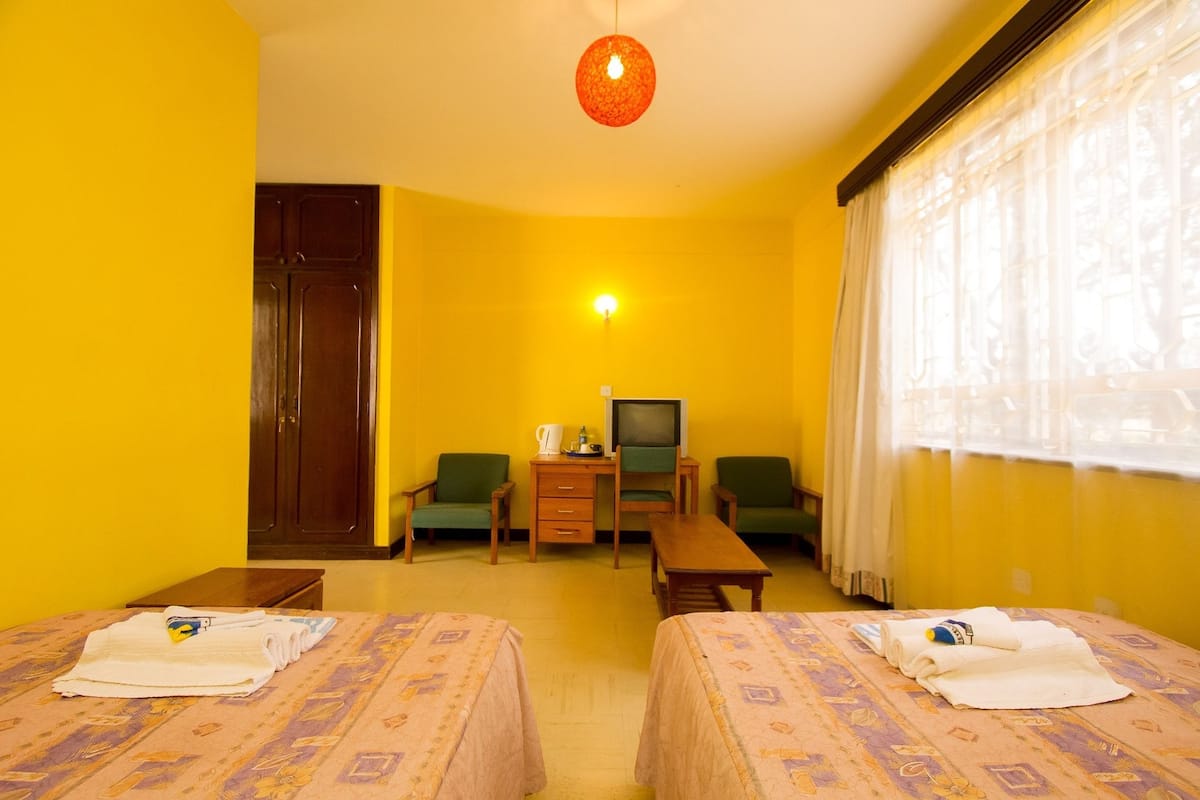 Habitación de hotel con dos camas, un escritorio con televisor y ventana con cortinas.