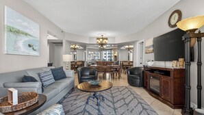 A spacious living room with a grey sofa, a coffee table, and a TV on a wooden cabinet. - FREE Beach SRVC! Free Beach Bonfires M/F! Ocean Views! (Miramar Beach)