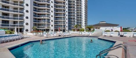 A swimming pool with lounge chairs and a high-rise building in the background.