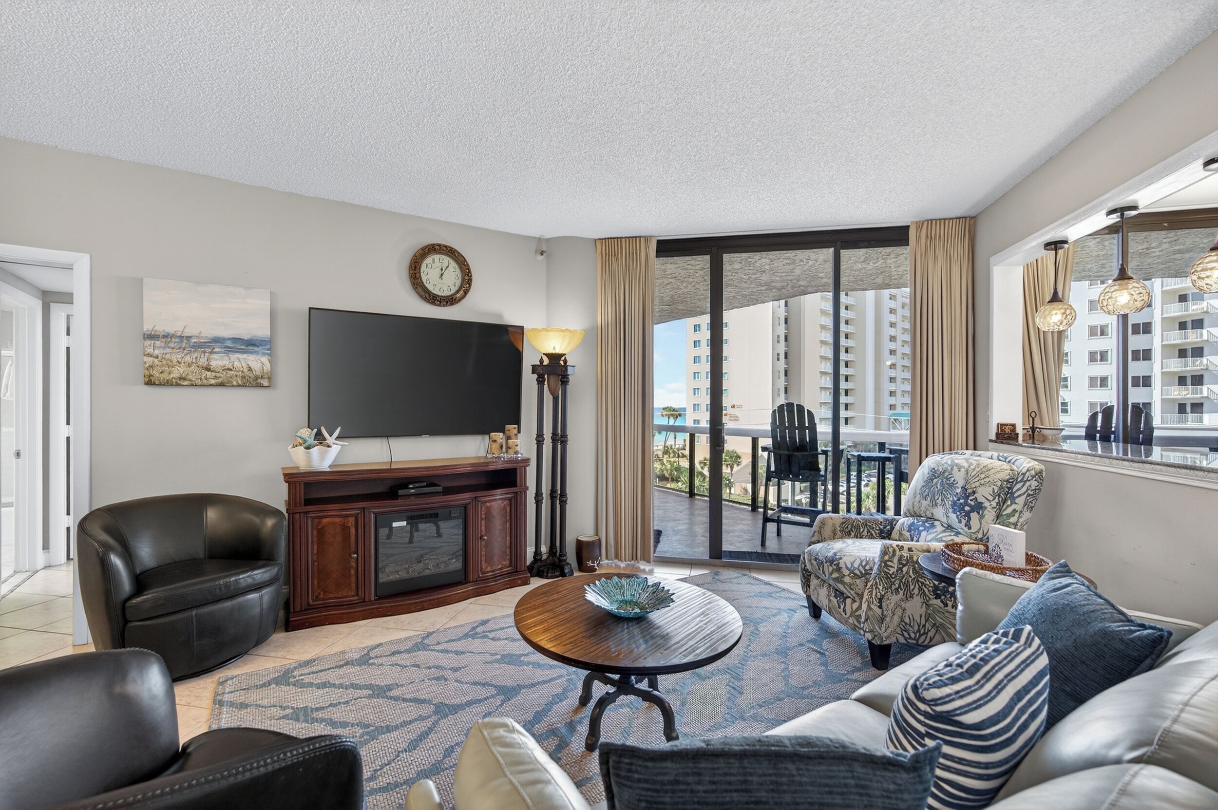 A modern living room with a flat-screen TV, a coffee table, and a sofa. There is a balcony with a view of high-rise buildings.