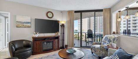 A modern living room with a flat-screen TV, a coffee table, and a sofa. There is a balcony with a view of high-rise buildings.