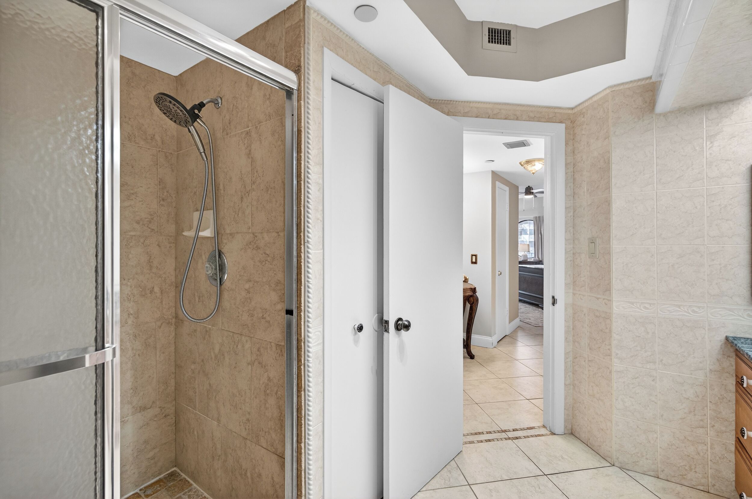 Une salle de bain moderne avec une douche à l’italienne, une porte blanche et un couloir menant à un espace cuisine.