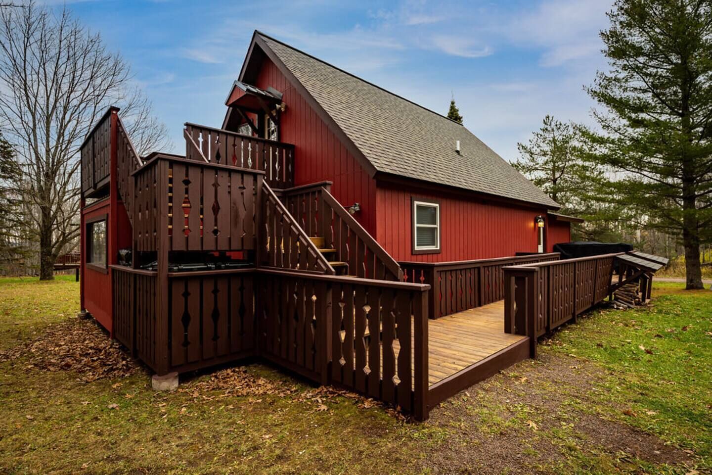 A red wooden cabin with a wooden deck and stairs leading to a loft area.