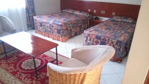 A room with two beds, a small table, a wicker chair, and a red patterned rug.