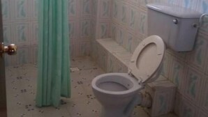 A bathroom with a toilet, a shower curtain, patterned tiles, and a window.
