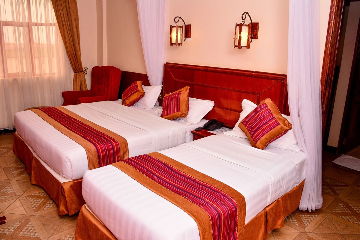 Une chambre d’hôtel avec deux lits, chacun recouvert d’une couvre-lit à rayures rouges et blanches, doté d’une tête de lit en bois et muni d’un téléphone sur la table de chevet.