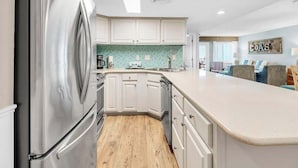 A modern kitchen with white cabinets, a stainless steel refrigerator, a wooden floor, and a light blue backsplash. - 407- Coastal Heaven Retreat - Upscale Beachfront, Truly Beautiful! (Destin)