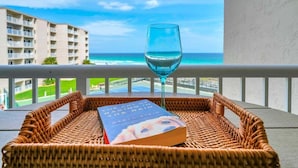 A wicker basket with a book and a glass of water on a balcony overlooking a beach and hotel buildings. - 407- Coastal Heaven Retreat - Upscale Beachfront, Truly Beautiful! (Destin)