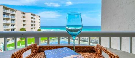 A wicker basket with a book and a glass of water on a balcony overlooking a beach and hotel buildings.