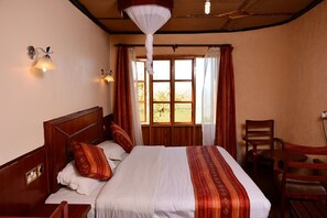 A hotel room with a wooden bed, a nightstand, a chair, and a window with curtains.