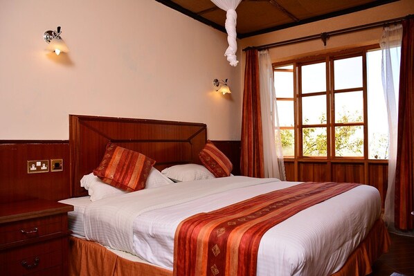 A neatly made bed with a wooden headboard, a bedside table with a lamp, and a window with curtains.