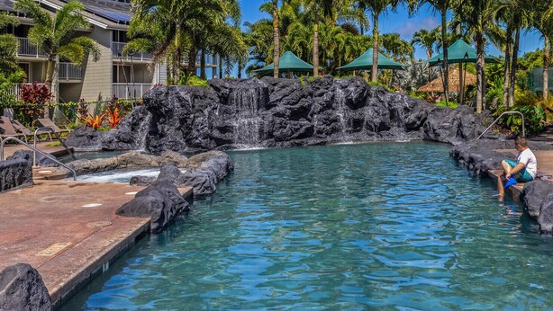 A pool with a rocky waterfall feature, surrounded by lounge chairs and palm trees. - CLIFFS 4-207,  SPECTACULAR VIEWS - 2 PRIVATE LANAIS AT THIS REMODELED CONDO (Princeville)