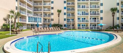 Un hotel con piscina rodeada de sillas de descanso y sombrillas.