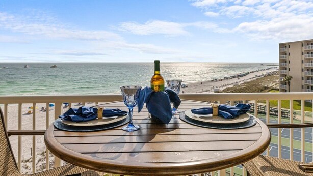 A table set for two with a bottle of wine, two wine glasses, and a blue cloth on a balcony overlooking a beach. - 522- Beachy Perfection at Holiday Surf and Racquet Club (Destin)