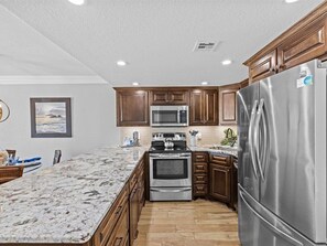 A modern kitchen with wooden cabinets, stainless steel appliances, and a marble countertop.