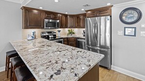 A kitchen with dark wood cabinets, stainless steel appliances, a marble island, and recessed ceiling lights. - 522- Beachy Perfection at Holiday Surf and Racquet Club (Destin)