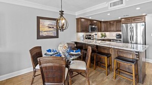 A modern kitchen with wooden cabinets, stainless steel appliances, and a dining area with wicker chairs. - 522- Beachy Perfection at Holiday Surf and Racquet Club (Destin)