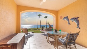 A sunlit patio with a view of the ocean, featuring a table, chairs, and a decorative dolphin mural.