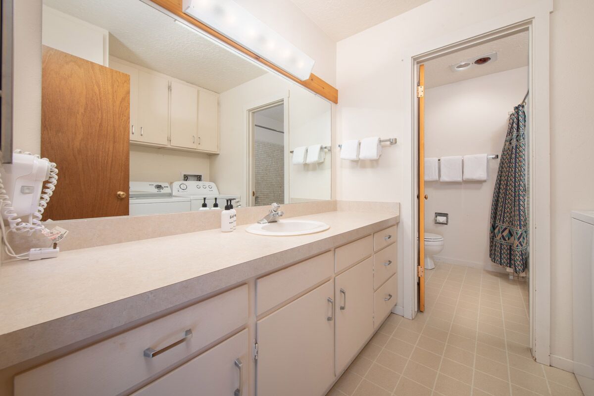 Un baño con lavamanos, espejo y toallero.