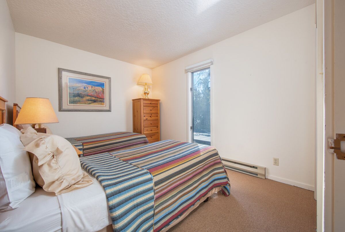 A bedroom with a bed, a nightstand, a lamp, a dresser, and a window.