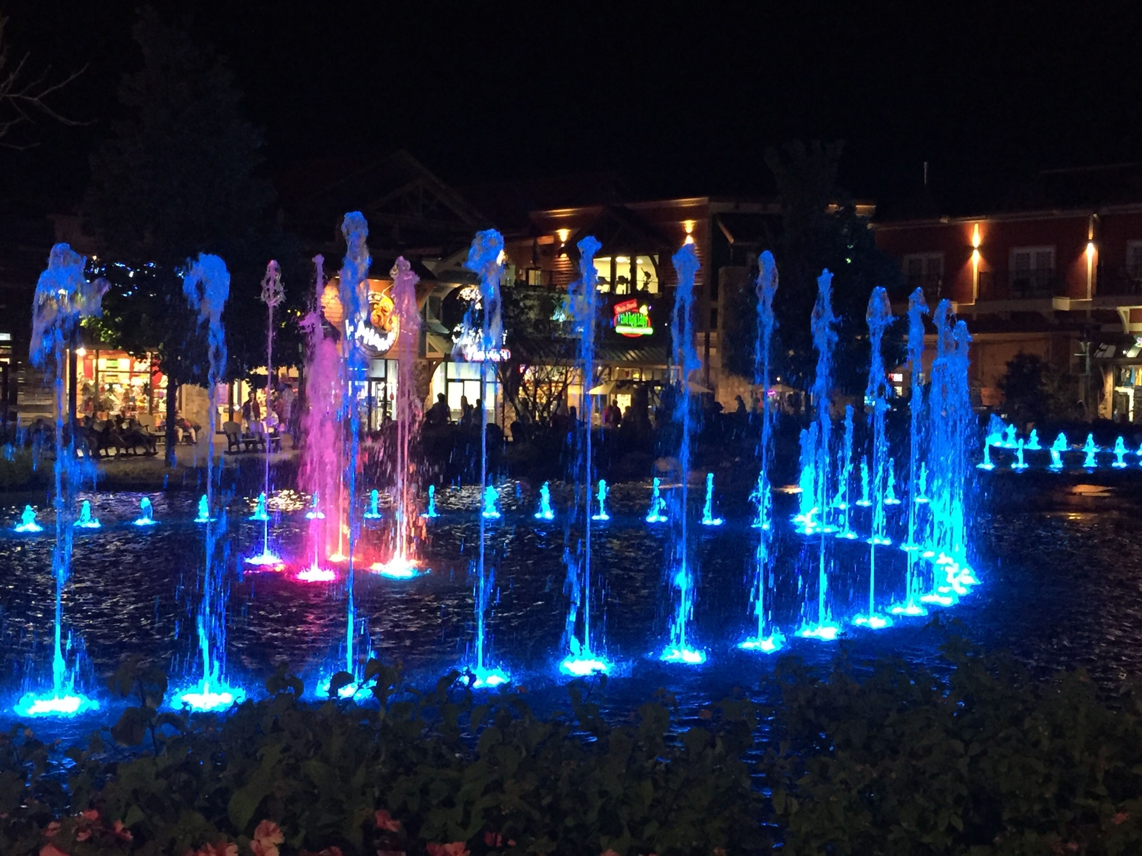Une fontaine illuminée de couleurs bleues et roses, avec de nombreux jets d’eau, qui offre un spectacle nocturne.