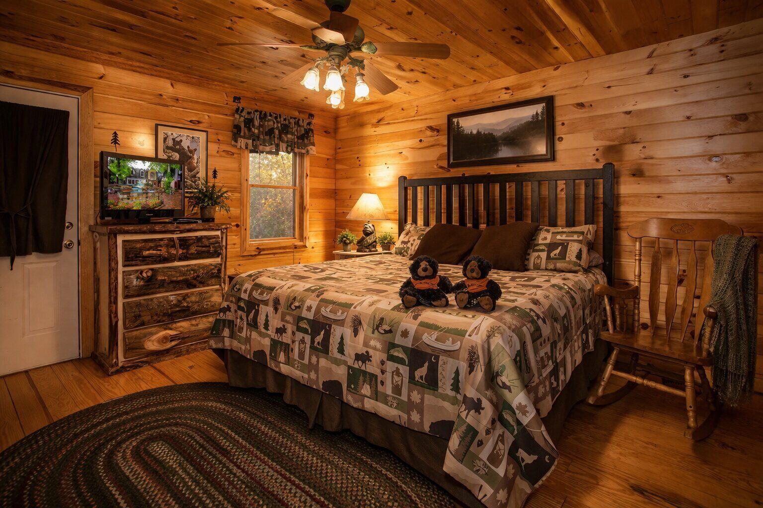Een gezellig, chalet-achtig vertrek met een houten plafond, een bed met een geborduurde deken, een televisie op een dressoir en een raam met uitzicht op bomen.