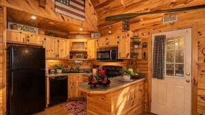 L’intérieur d’une cabane en bois comprend une cuisine équipée d’un réfrigérateur noir, d’un four à micro-ondes et de meubles de rangement en bois.