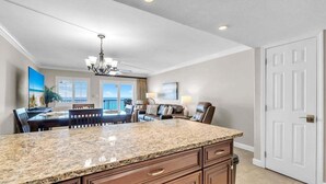 A kitchen with granite countertops, wooden cabinets, a chandelier, and a dining area with a view. - 603- Gulf Front with the Best Sunrise View, Plus FREE Beach Service (Destin)