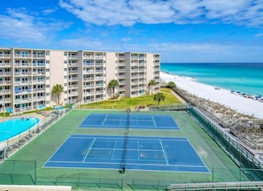 A multi-story hotel with a tennis court and pool, beachfront view.