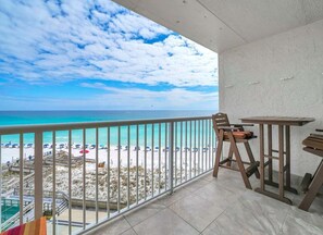 A balcony with a view of the beach and ocean, equipped with a table and chairs.