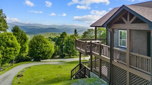 A wooden cabin with a balcony overlooking a lush green landscape and distant mountains. - Aussies Lookout - Panoramic Mountain Views, Hot Tub, Pool Table! (Blowing Rock)
