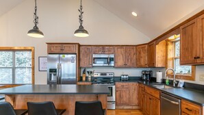 A modern kitchen with wooden cabinets, stainless steel appliances, a central island with bar stools, and pendant lighting. - Aussies Lookout - Panoramic Mountain Views, Hot Tub, Pool Table! (Blowing Rock)