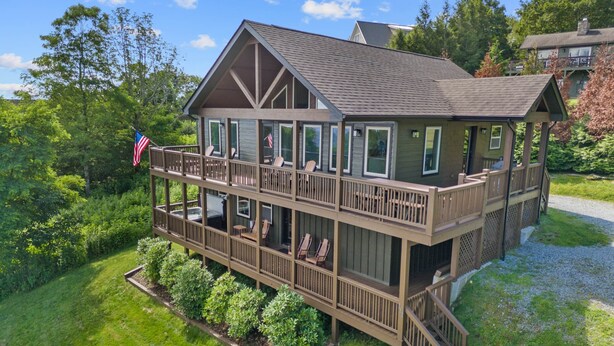 A two-story wooden house with a balcony, surrounded by lush greenery and a flag. - Aussies Lookout - Panoramic Mountain Views, Hot Tub, Pool Table! (Blowing Rock)