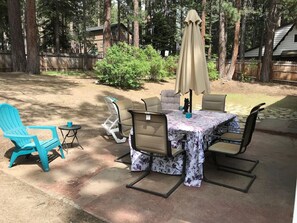 An outdoor patio with a table and chairs, surrounded by trees and a wooden fence.