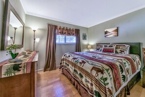 A bedroom with a bed, a nightstand, a dresser, a window with curtains, and a wall-mounted lamp.