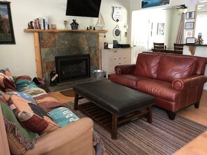 A living room with a fireplace, leather sofa, ottoman, and a colorful blanket.