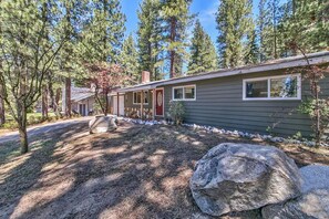A single-story house with a dark siding exterior, a red door, and a small porch area. - The Peace of Heaven Home Has Been Lovingly Set Up (South Lake Tahoe)
