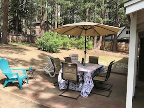 An outdoor patio with a table and chairs, a blue Adirondack chair, and a large umbrella.