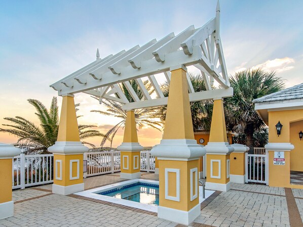 A pool area with a pergola, palm trees, and a sunset in the background.