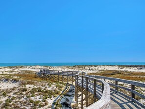 Een houten vlonder die naar een strand leidt, met helderblauwe lucht.