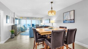 Un coin repas comprenant une table en bois, six chaises, un lustre et un tableau représentant un voilier accroché au mur.