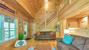 Ein Holzblockbau-Innenraum mit Treppe, zwei Sofas, einem Couchtisch und einem großen Fenster.