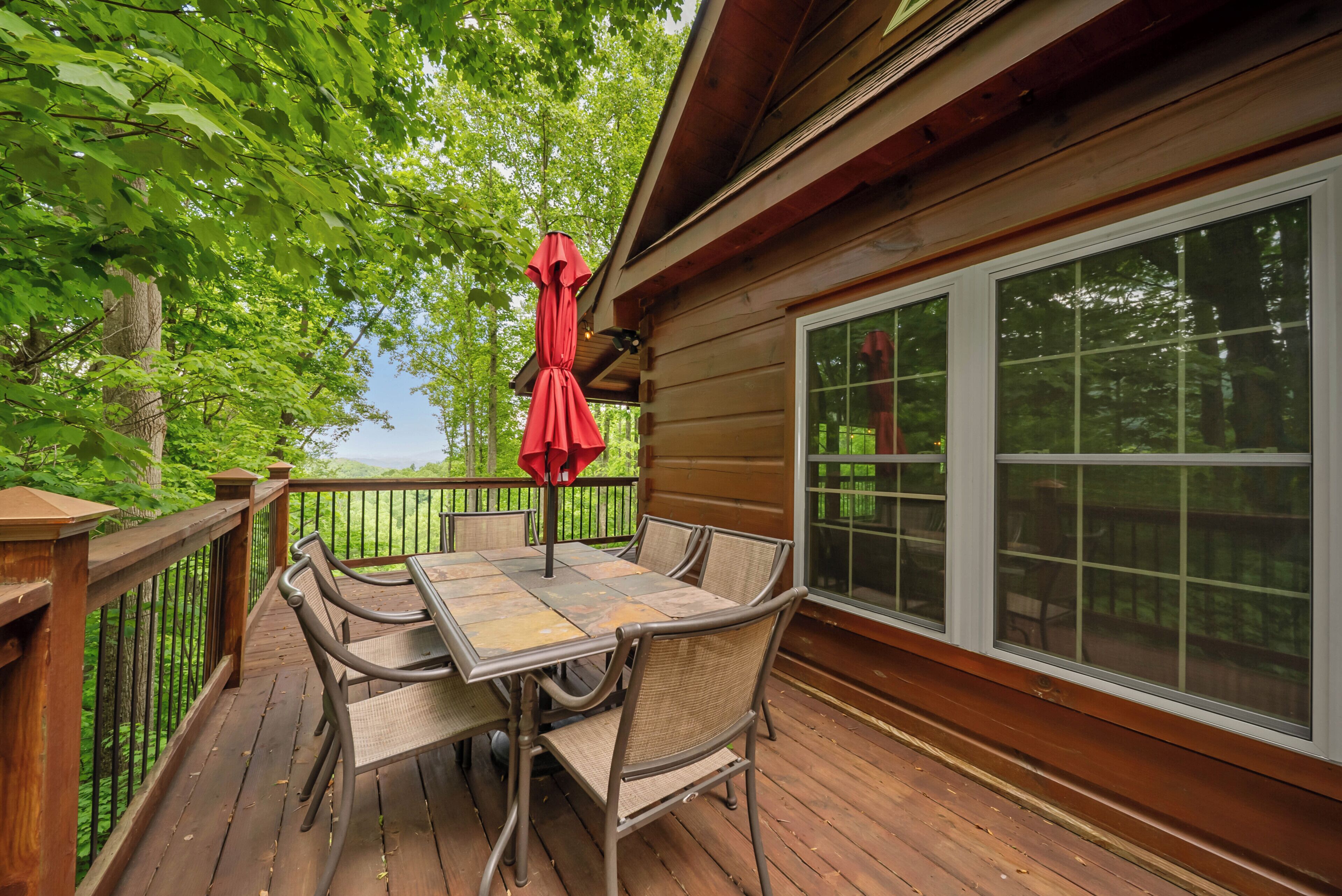 A wooden deck with a table and chairs, a red umbrella, and a large window.