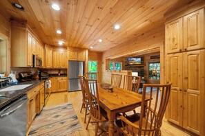 A wooden cabin interior with a kitchen, dining area, and a fireplace.