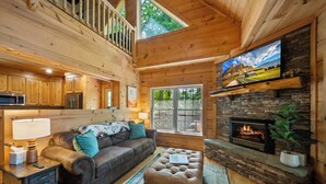 Ein Holzblockhaus-Interieur mit Kamin, Fernseher, Sofa und Essbereich.